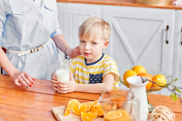 Mother and son are smiling while having a breakfast in kitchen. Mom is pouring milk into glass