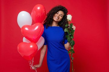 pretty black woman with white rose and heart shaped colorful balloons isolated on red background