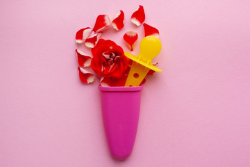 Red rose and petals in a glass for ice cream on a pink background. Space for text. flower composition