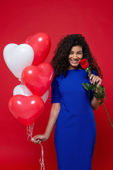 happy black woman with heart shaped balloons and rose isolated on red background
