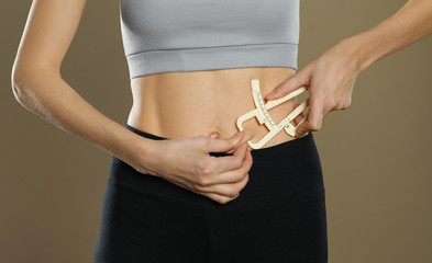 Young woman measuring body fat with caliper on beige background, closeup