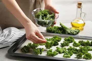 Poster Woman preparing kale chips at table, closeup © New Africa