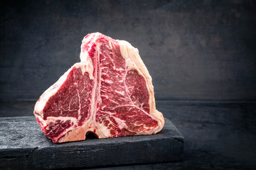 Fototapeta Raw dry aged wagyu porterhouse beef steak with large fillet piece as closeup on a black burnt wooden board with copy space right obraz