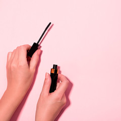 Woman hands holding open black mascara on pastel pink background, top view. Minimal beauty background with makeup products, flat lay, copy space. Eye make up concept