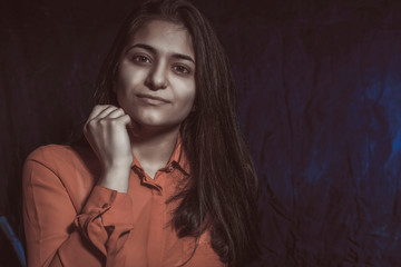 portrait of a beautiful indian woman holding her hand to her chin, calm emotion. on a dark blue background. In artistic tinting