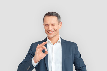 Freestyle. Mature businessman standing isolated on white showing ok gesture winking to camera...