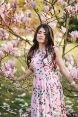 Charming girl stand by the beautiful pink magnolia tree outside. Gorgeous lady