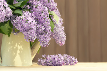 Vase in the form of an old vintage watering can with a bouquet of lilacs on table on a wooden background