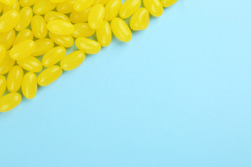 Many delicious lemon jelly beans on light blue background, flat lay. Space for text