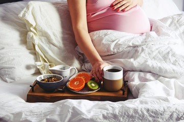 Fototapeta na wymiar Pregnant woman is having a healthy breakfast in bed. Pregnant woman in a bed on white linen background