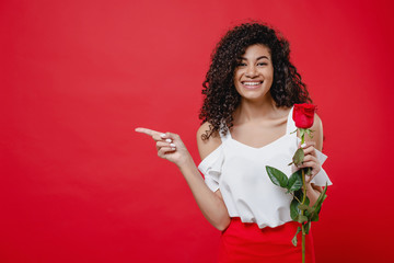black woman with rose in hand pointing finger at copy space isolated over red