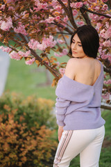 Attractive young woman in a purple sweater stand in front of sakura tree in the park