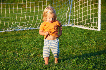 Child baby girl playing on soccer field near goal in sunset light