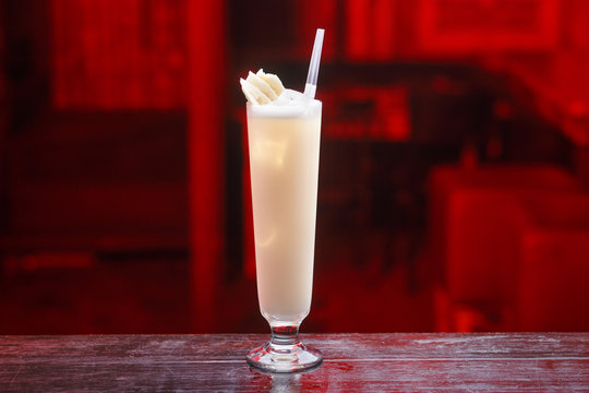 Closeup of a long glass of pinacolada cocktail, standing on the bar counter, isolated on a red light background. Horizontal view.