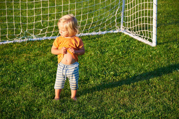 Child baby girl playing on soccer field near goal in sunset light