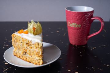 Slice of carrot cake with sour cream sauce and walnuts, garnished with physalis and a cup of coffee