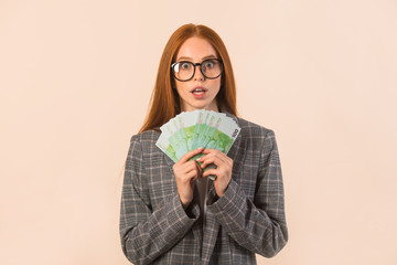beautiful young woman with red hair in a jacket on a beige background with euro in hands