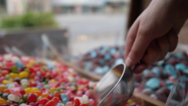 Close-up of man's hand taking colourful candies with scoop. Box with many different sweets