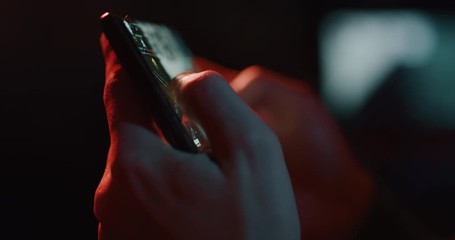 Cinematic close up shot of an young man gamer is using a smartphone for playing a video games isolated on a dark background. - Powered by Adobe