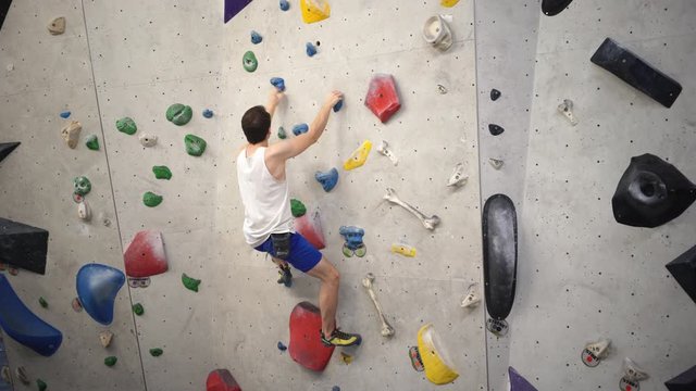 athletischer Mann beim Bouldern klettert eine leichte Route an Kletterwand