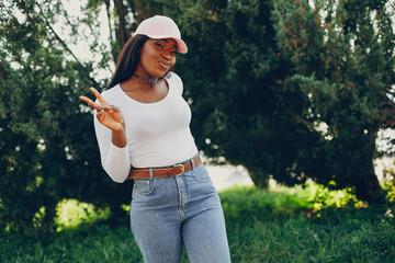 Stylish girl in a summer park. Woman in a blue jeans and pink cap