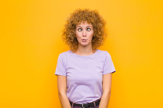 young afro woman looking goofy and funny with a silly cross-eyed expression, joking and fooling around against orange wall