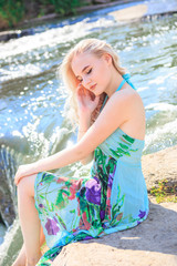 Young blonde in a dress on the bank of a bubbling river