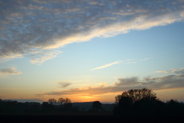 Sunset with trees silhouette, blue sky and gray clouds.