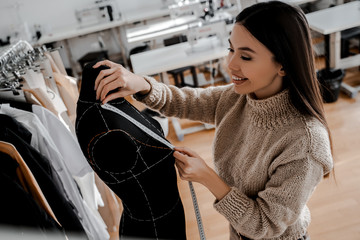 Beautiful woman tailor, fashion designer, sewing mannequin, adjusting blouse. Her studio is bright...