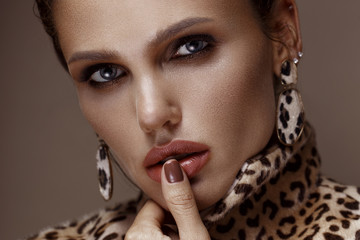 Beautiful sexy woman in a leopard coat and earrings, with classic smokey makeup and a fashionable...