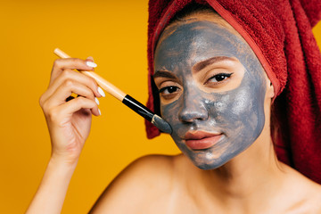 girl with a towel around her head makes a black mask with a cosmetic brush