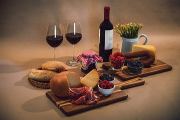 Table with a variety of gourmet ingredients, cheeses, cold meats, serrano ham, wine glass, grapes and artisanal bread served on the wooden table with a rustic background.