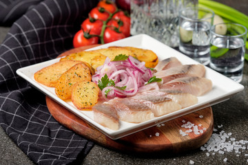 White plate of pieces of pickled herring, chopped chives with fried potato, onion, tomato and cold vodka. Russian traditional cuisine. Close up.