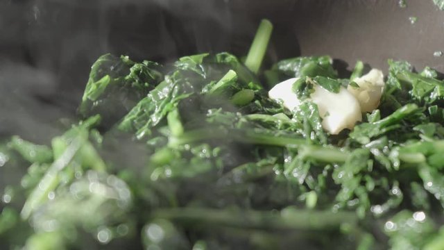 Close up of chicory vegetables that fry in the pan with garlic with the steam of cooking