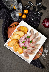 White plate of pieces of pickled herring, chopped chives with fried potato, onion, tomato and cold vodka. Russian traditional cuisine. Close up.