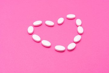 White oval pills lie on a pink background. Copy space, macro