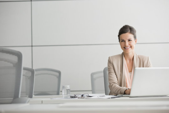 Smiling businesswoman working at laptop in conference room