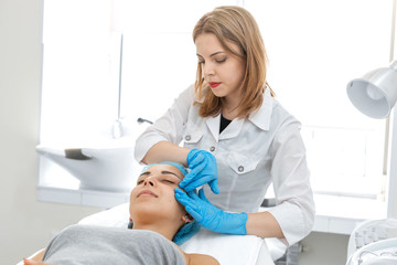 Fototapeta premium Beautician makes a young beautiful girl a relaxing and wellness facial massage. Facial care and rejuvenation.