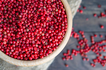 Close up view of pink peppercorn ("Brazil Pepper" or "Schinus terebinthifolius") in wooden bowl, dark rustic background. Flat lay, top view. Hot organic spices concept.