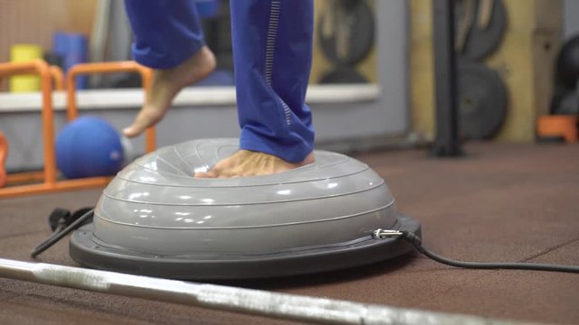 Man trains balance, balances on simulator, bosu