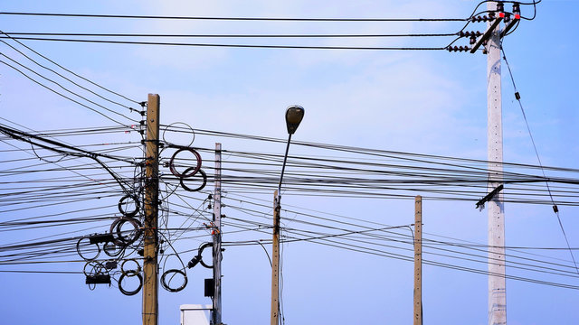 Messy electrical cable lines and wires on power pols against cloud and blue sky background.