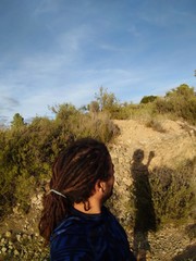 European man with dreadlocks in the mountain , sefie with his shadow.