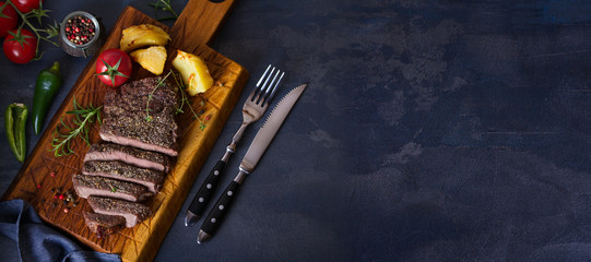 Grilled fillet beef steak with potatoes on serving board. View from above, top view. Copy space