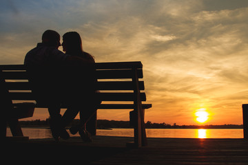 A romantic male and female couple embrace lovingly while sitting on a beach in front of a magical sunset over the water