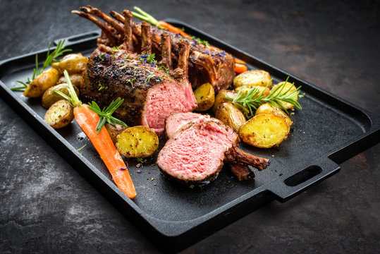 Barbecue rack of lamb with carrot and potatoes offered as closeup on a modern design cast iron tray