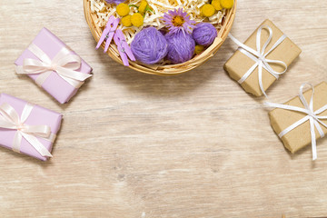 Fototapeta na wymiar Flat lay of flowers, petals, leaves and gifts. Holiday yellow, purple and white decor on the wooden table. 