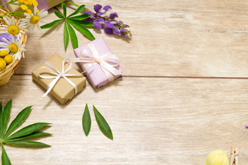 Presents in violet and kraft paper on the wooden table. Purple, white and yellow flowers lay around.