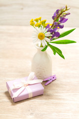 Obraz na płótnie Canvas Purple flowers as a present on the table. Violet gift wrapped in paper and pins. Chamomiles, yellow and green plants