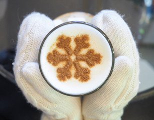 Сoffee latte with a pattern of snowflakes hold hands in white mittens. Warm and cozy winter concept.  Top view.