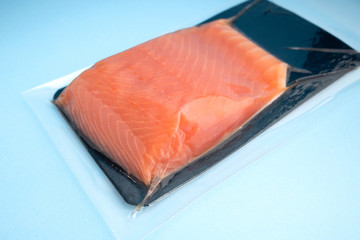 Raw Sea-fish steak packaged in plastic vacuum container. Top view of piece of raw salmon on blue background.